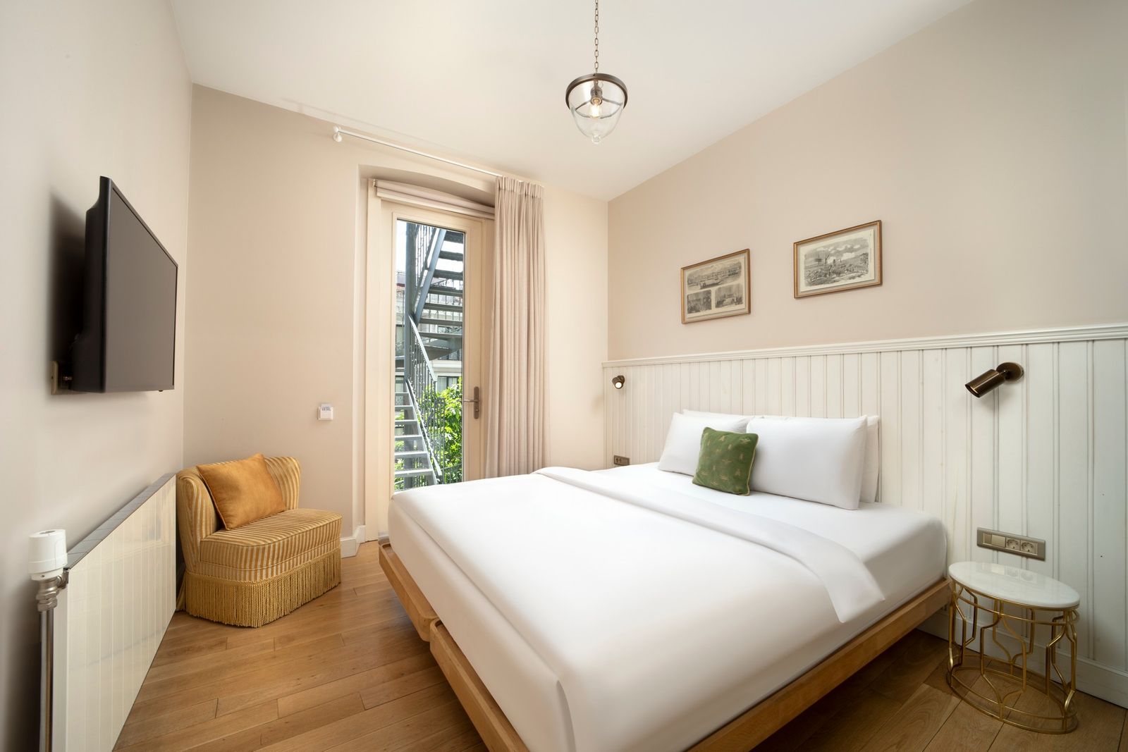 The bedroom of the One-Bedroom Apartment — king bed, linen headboard, the door to the small balcony just open.