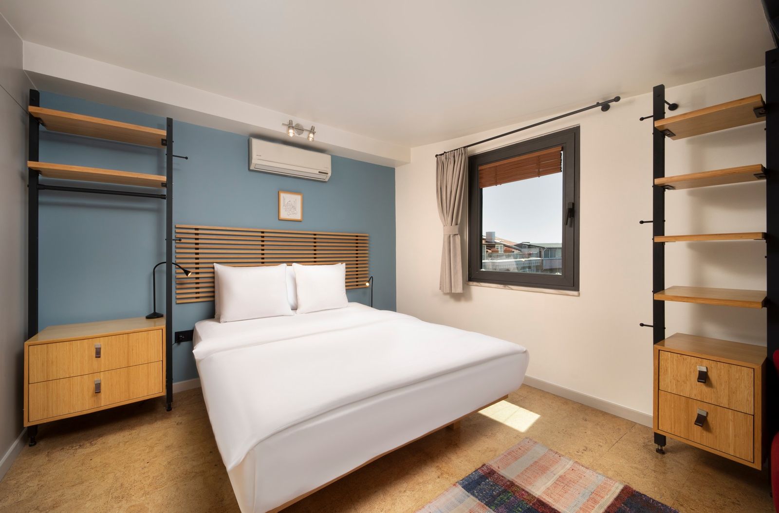 The bedroom end of the Terrace Suite — king bed against a soft plaster wall, two reading lights in brass.
