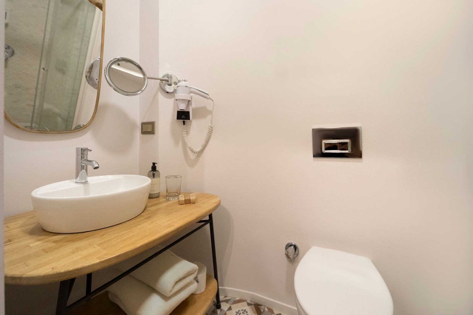 The compact bathroom of the Patio Room — frosted-glass partition, marble shower, brass fittings, a small folded towel on a wooden bench.