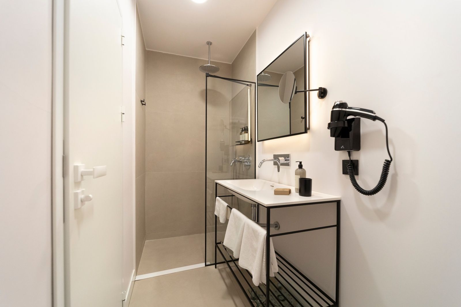 The compact bathroom of the Studio Flat — frosted-glass partition, pale marble shower, brass rain head.