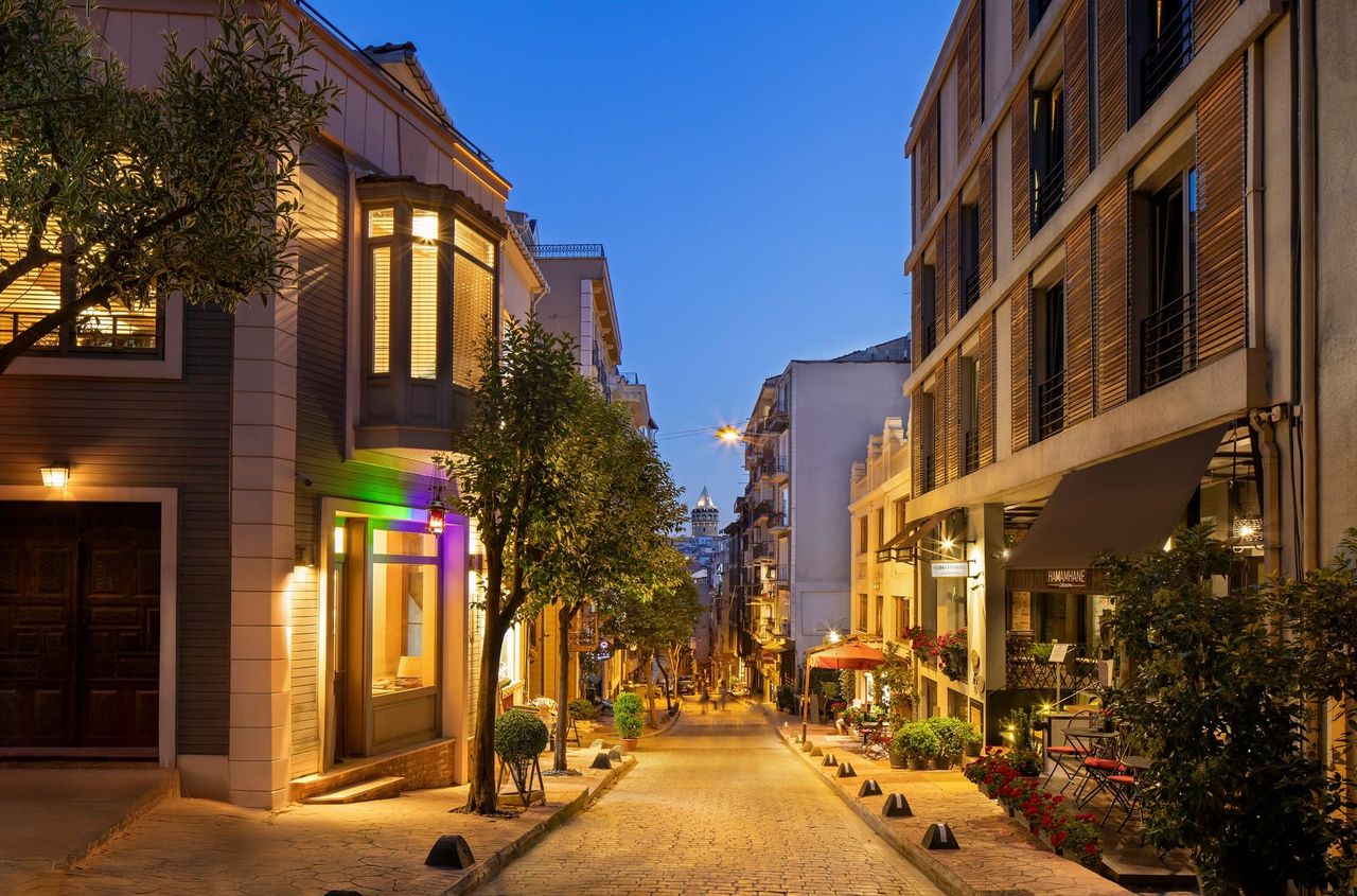 Çukurcuma Street at dusk — soft amber lamps, the silhouette of the hamam dome at the end of the lane.