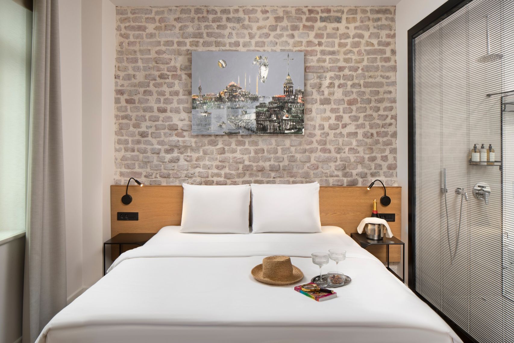 The bedroom corner of the Superior Studio — an exposed-brick wall, a low headboard in natural linen, a single brass reading light.