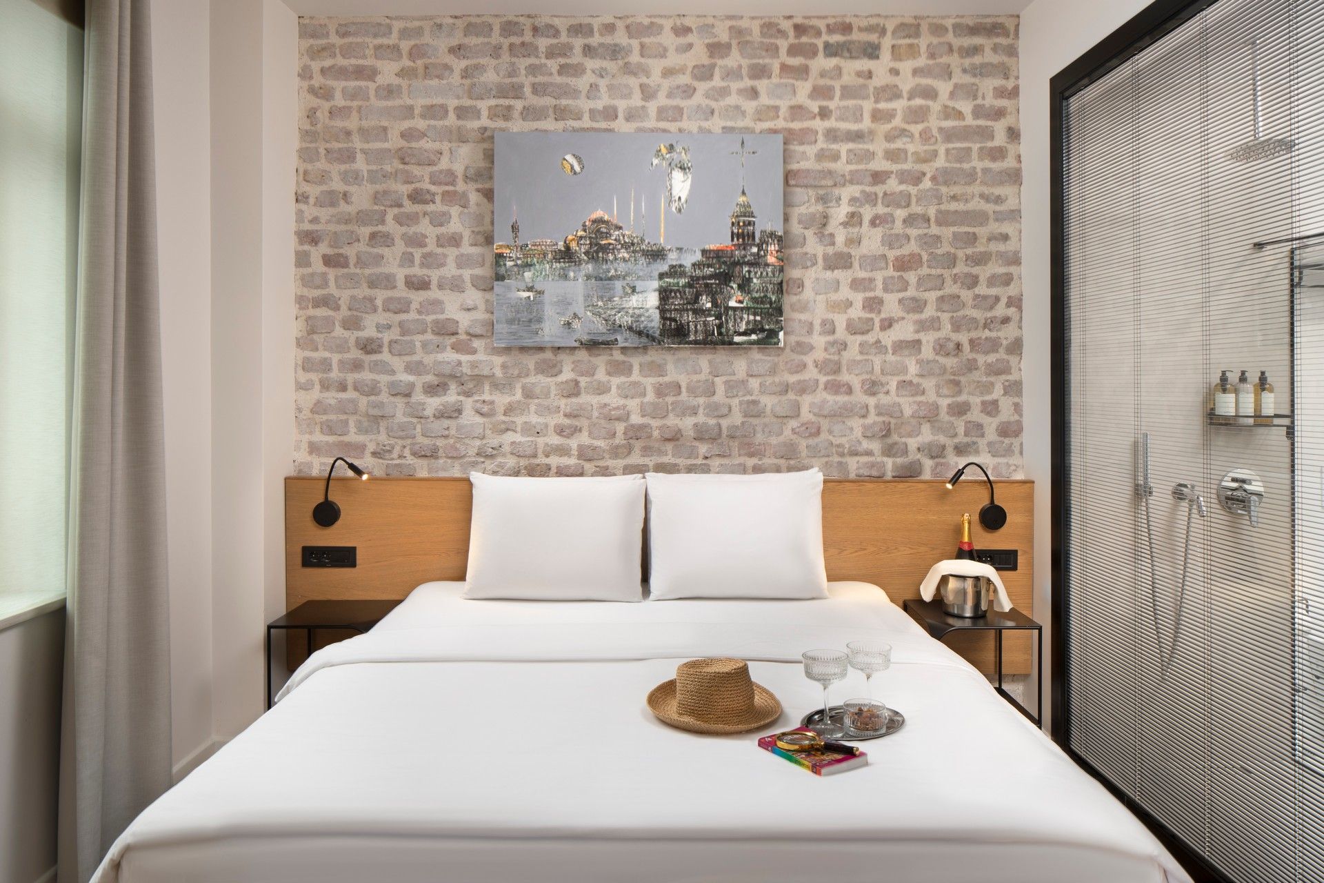 The Superior Studio bedroom corner — exposed-brick wall, low linen headboard, a single brass reading light.