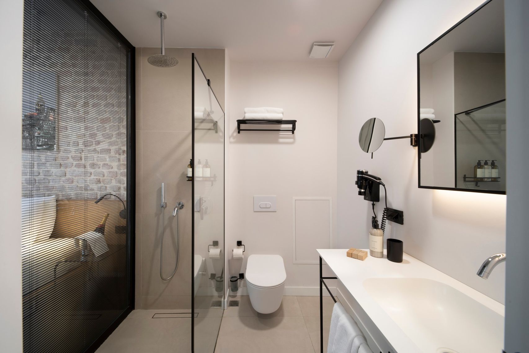 The walk-in bathroom — pale marble, brass fittings, a rain shower set behind frameless glass.